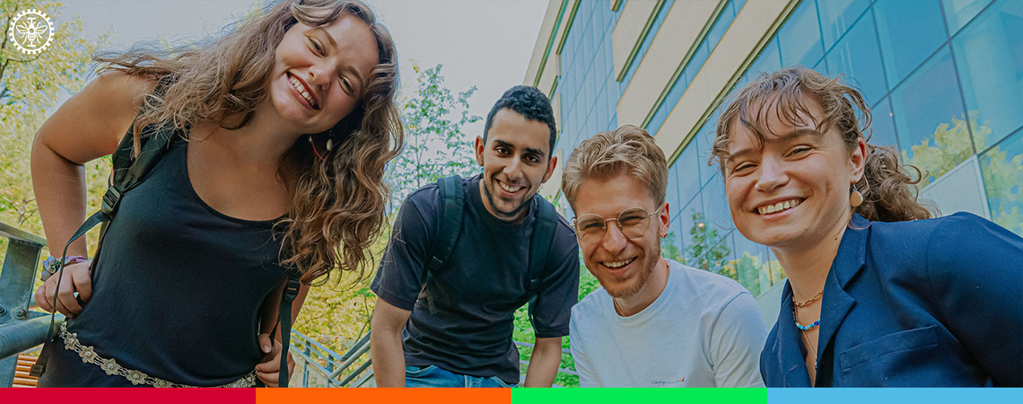 Quatre étudiantes et étudiants souriants, se penchent vers la caméra devant Polytechnique Montréal.